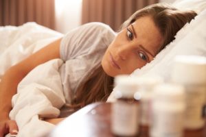 woman in bed looking at multiple pill bottles on bedside table and wondering the signs of pain pill abuse