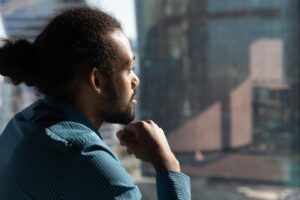 a man looks out the window wondering the difference between social drinking vs alcoholism