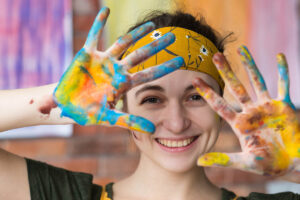 a woman smiles with her hands up showing paint all over her hands after her art therapy and mental health program