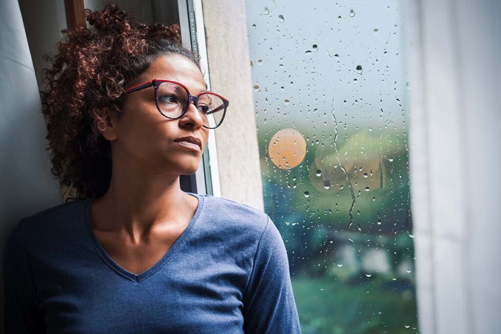 a woman leans on a window looking out and wondering about the common myths about addiction