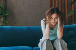a woman sits on a couch with her hands to the sides of her head appearing distraught as she deals with anxiety and substance abuse