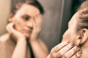 a woman looks at her reflection in the mirror while thinking about her struggle to deal with her addictive behaviors