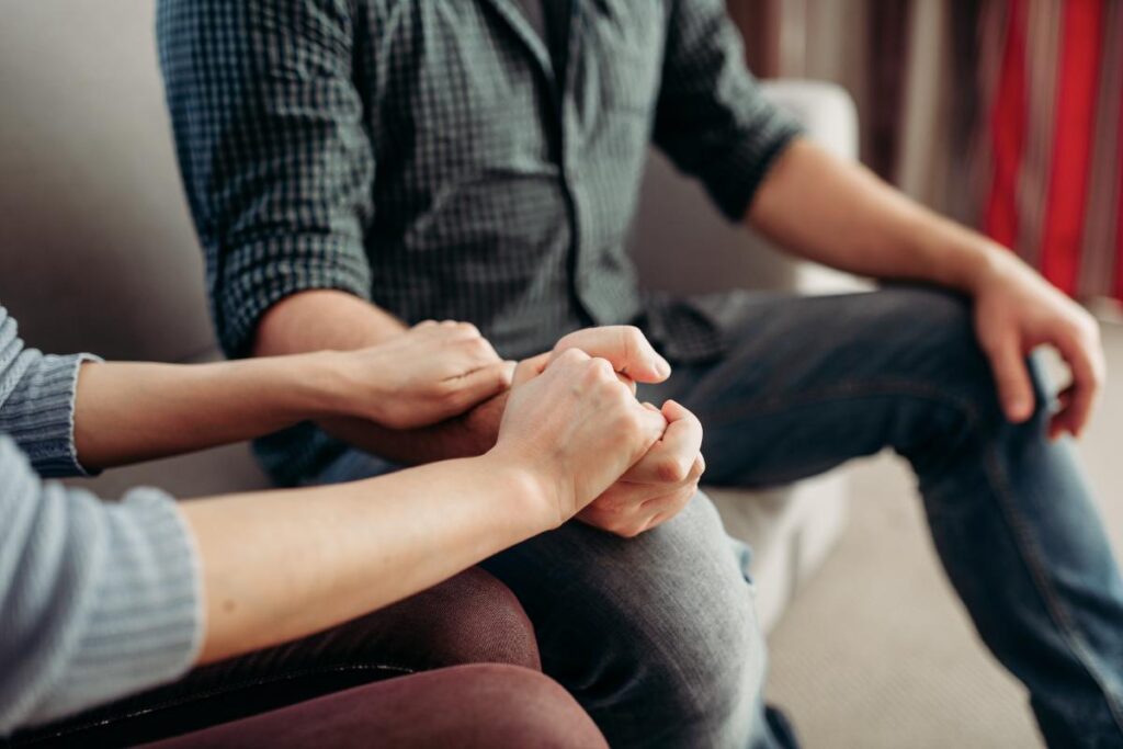 a person's hands hold onto a man's arm and hand while consoling him and discussing vicodin addiction treatment