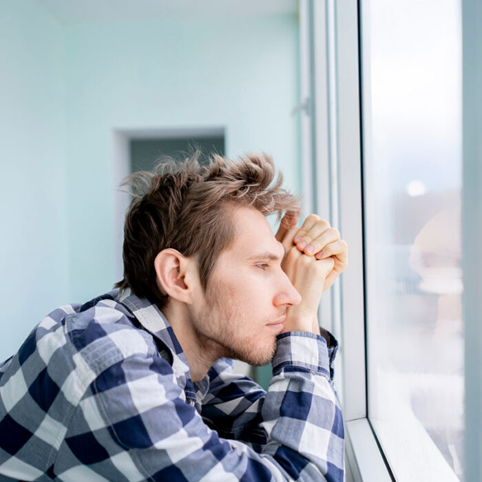 man in flannel looks out a window thinking deeply about the impact of trauma on the brain