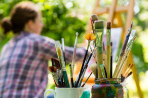 two jars full of paintbrushes near a woman who is painting and showing what is art therapy