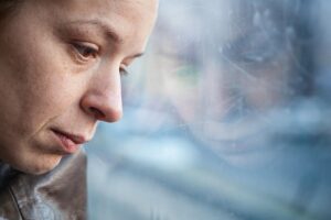 a sad woman looks out the window while thinking about the signs of xanax abuse