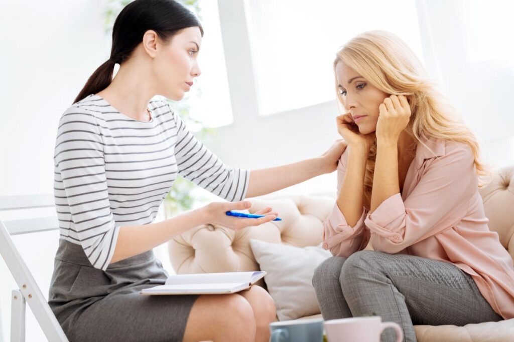 a woman therapist puts her hand her woman patient's shoulder to console her while talking to her about the benefits of a women's addiction treatment center