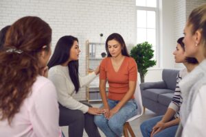 a woman sits with other women in a group therapy session in her gender-specific addiction treatment
