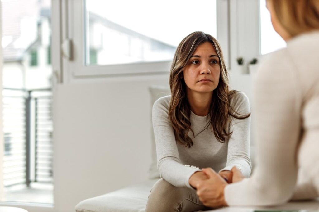 an adult woman sits and listen to a person across from her explain the benefits of cbt and mental health treatment