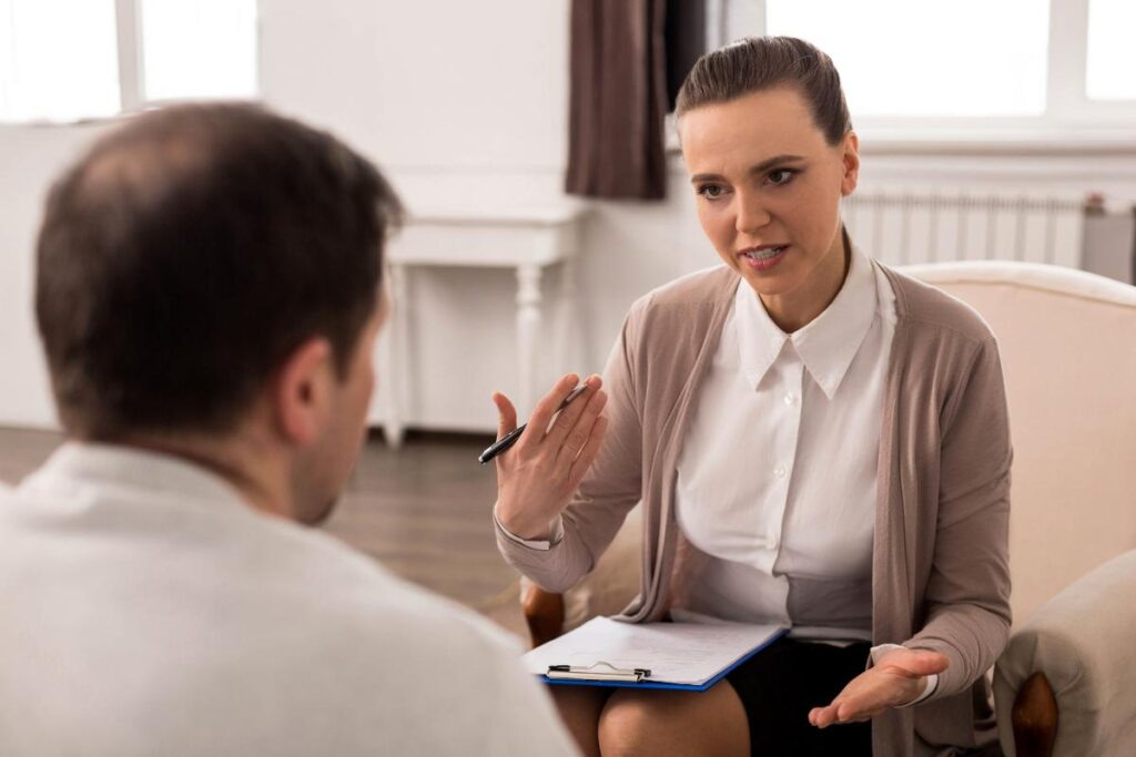 a woman sits with an adult man to discuss how to find a therapist